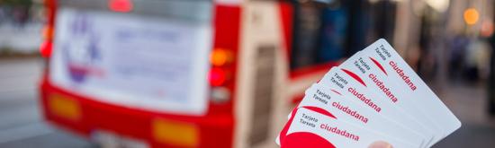 Hand holding Gijon's citizen card, a bus in the background.